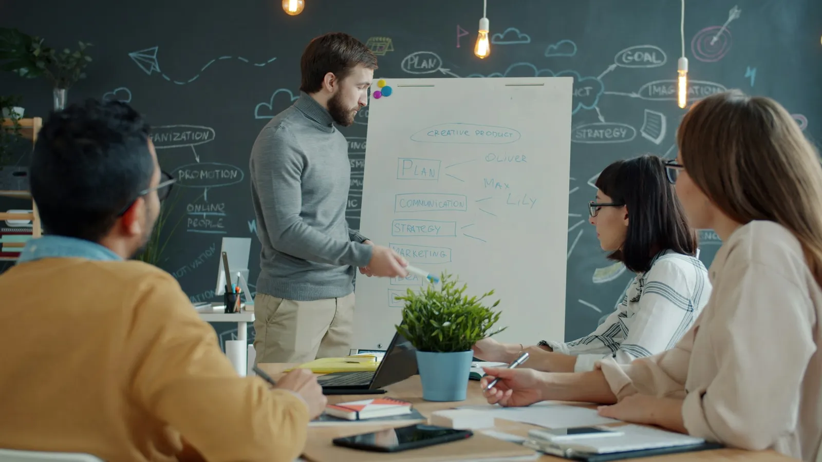 A man talks a small team through a strategy sketch on a flip chart while colleagues take notes.
